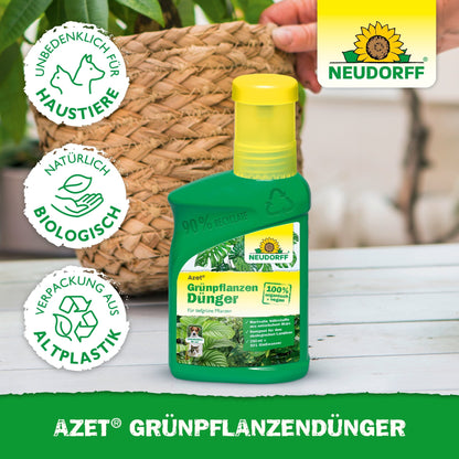 A green bottle of Neudorff Shop Azet Green Plant Fertilizer liquid stands on a table next to a potted plant. The label lists nutrients for green plants, pet safety, natural ingredients, and recycled packaging. A hand is visible in the background.