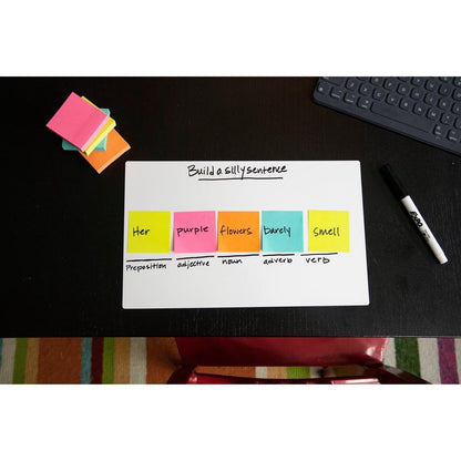 On a black desk stands a whiteboard with the inscription "Build a silly sentence". The Post-it® Notes Cube, Ultra Colors, 76x76 mm, by 3M Deutschland GmbH, display the parts of speech. Also on the desk: a dry-erase marker, a notepad, and a keyboard.