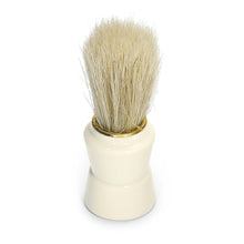 A shaving brush with light bristles and a white handle stands upright on a white surface, perfect for barbers or in combination with the Nölle Profi Brush Universal Comb 18 cm from Nölle Profi Brush Bürsten- & Pinseltechnik e.K. for professional results.
