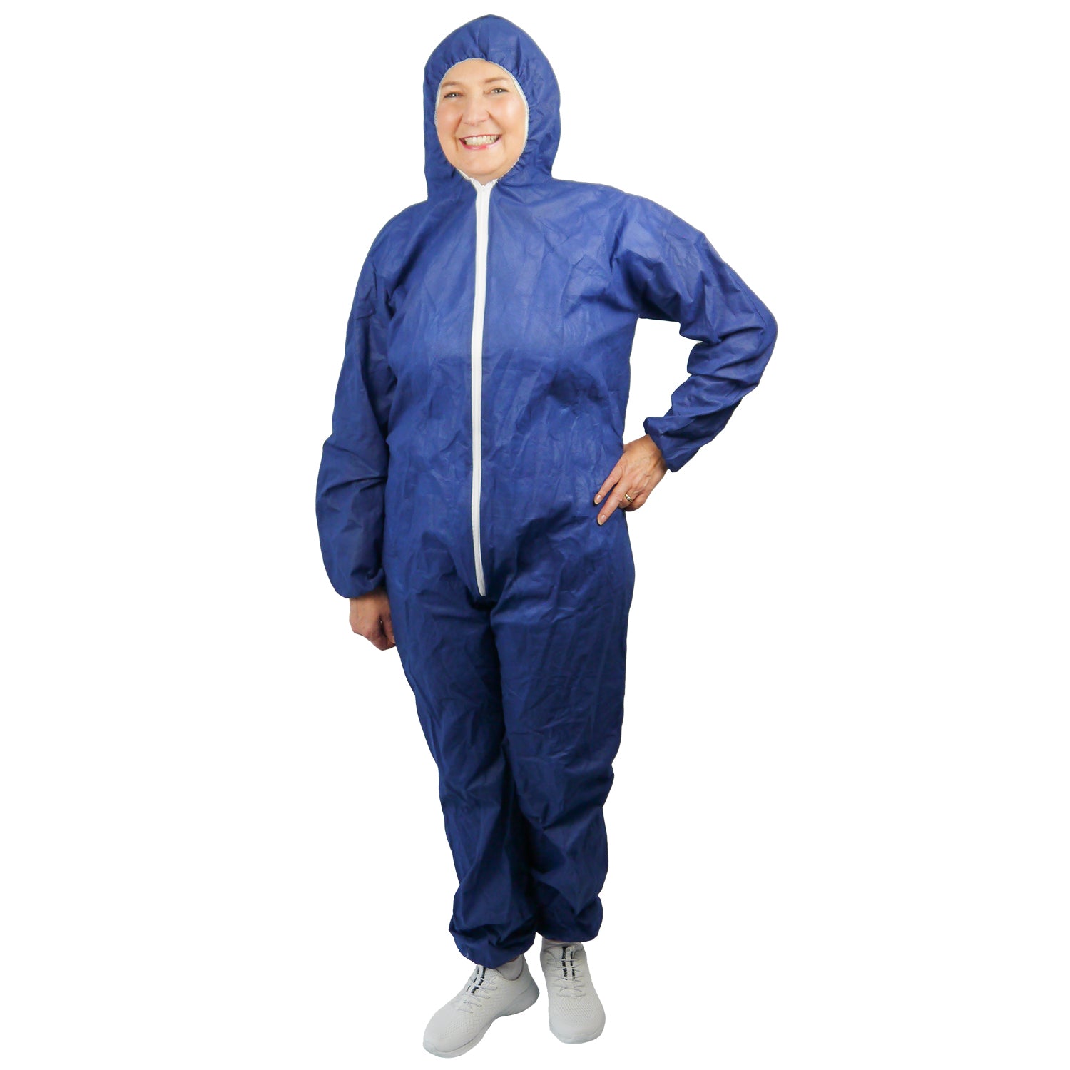 A person is standing smiling in an ARNOMED COVER PP-OVERALL XTRA STRONG by ARNOWA GmbH, a blue, extra strong disposable coverall with a hood and white front zipper, paired with white shoes, against a plain white background.