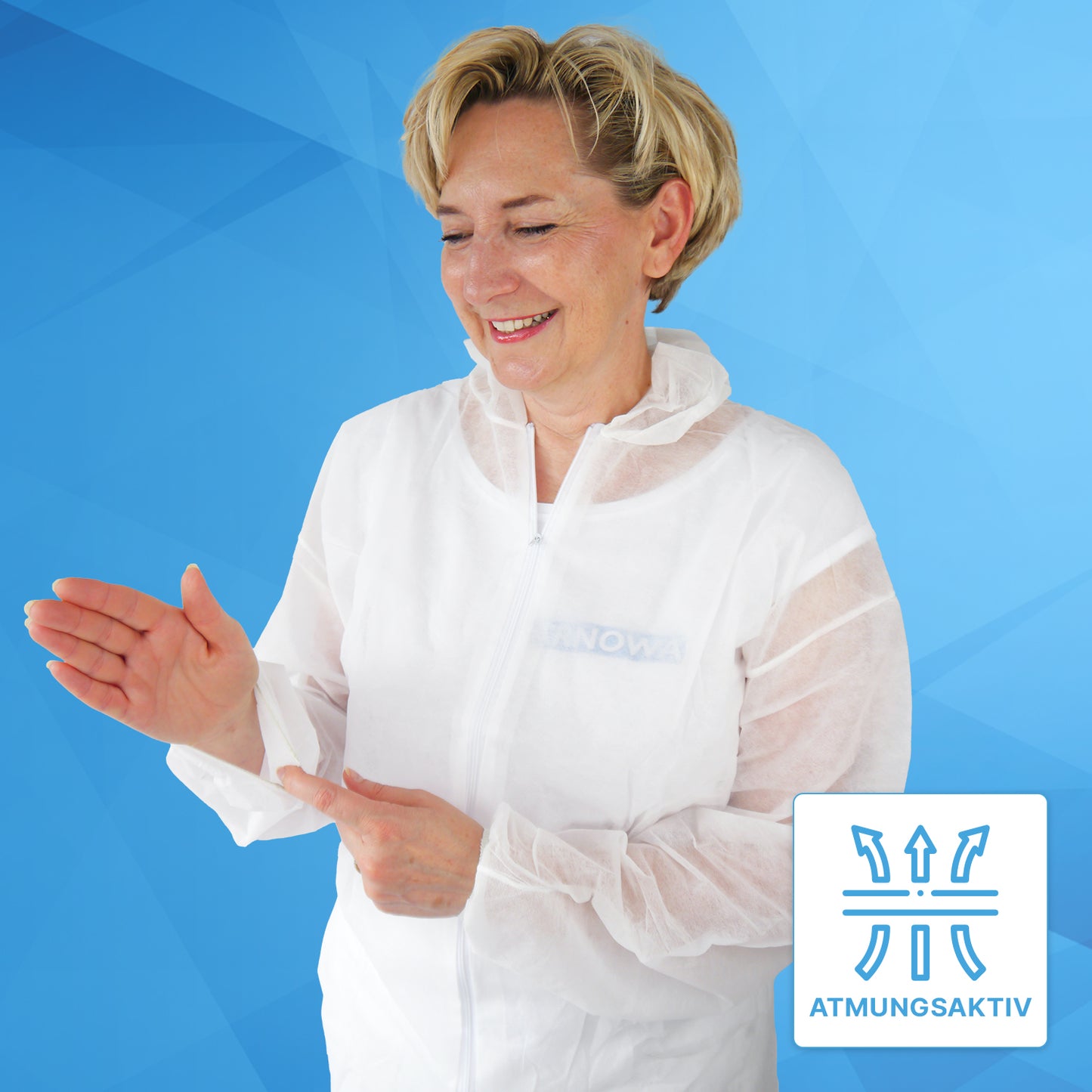 A woman in the ARNOMED COVER PP-OVERALL XTRA STRONG from ARNOWA GmbH stands in front of a blue background, smiling while adjusting her sleeve. A symbol with the inscription "BREATHABLE" indicates the breathability of the white disposable coverall.