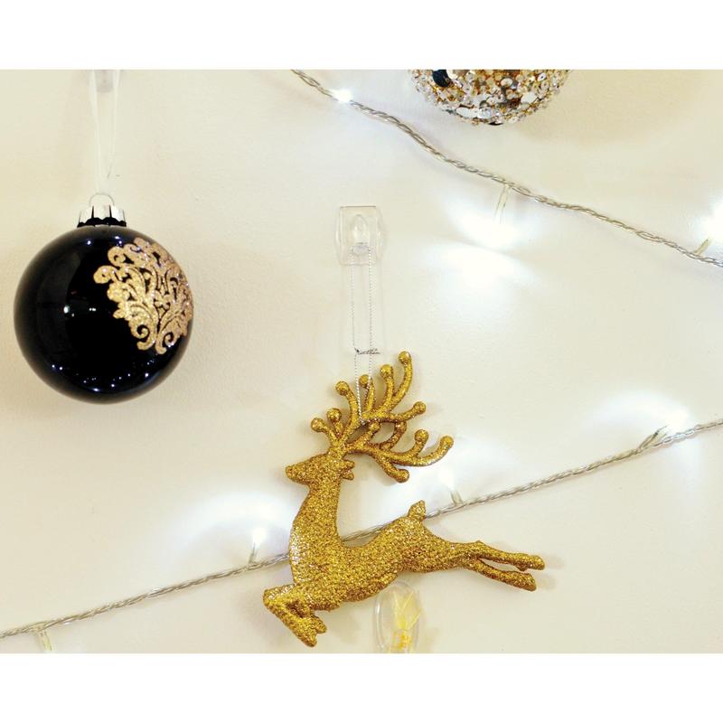 A golden glitter reindeer ornament hangs on a Command™ Mini Hook, transparent, with transparent strips (17006CLRFGN) by 3M Deutschland GmbH, with a black and gold Christmas bauble and white Christmas lights in the background.