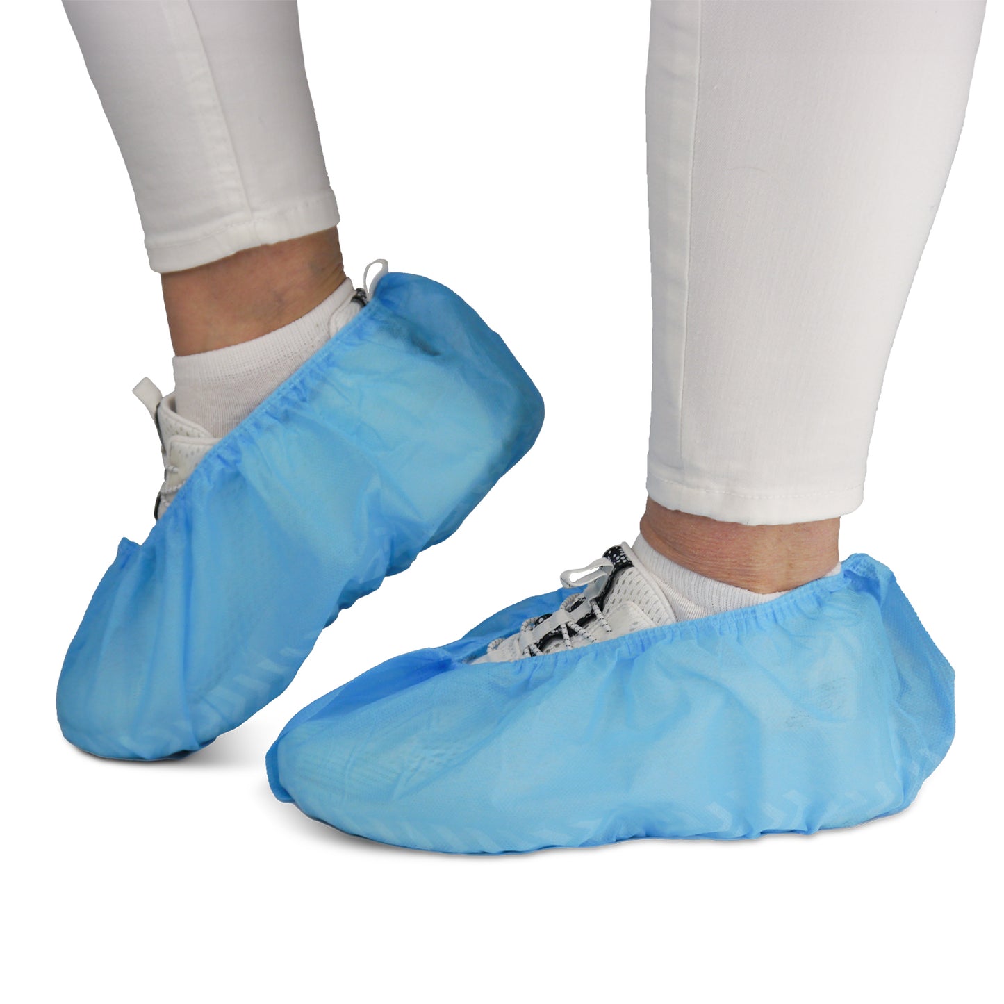 A person is wearing white pants and sneakers with ARNOMED ABS shoe covers from ARNOWA GmbH. These non-slip, disposable shoe covers (pack of 100) protect shoes and floors—ideal for hygienic environments.