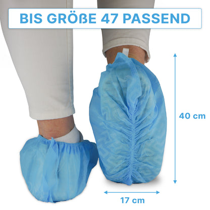 A person is wearing blue ARNOMED ABS shoe covers from ARNOWA GmbH over white pants; these non-slip, disposable shoe covers fit up to size 47 and measure approximately 40×17 cm, as indicated by the arrows. Package: 100 pieces.