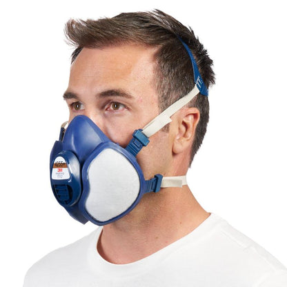 A man with short brown hair wears a blue-white 3M™ respirator with integrated filters from 3M Deutschland GmbH with adjustable straps, depicted against a plain white background.