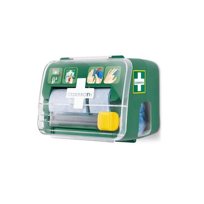 A green, transparent Cederroth 2-in-1 soft foam bandage dispenser from Orkla Wound Care AB is mounted on a white wall; it holds the packaged bandages and features illustrated first-aid instructions on the front.