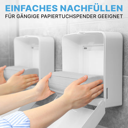 A person refills a white dispenser with ARNOMED PAPER TOWELS 25 x 23 cm | V-FOLD from ARNOWA GmbH. Another identical dispenser stands next to it. The German text describes the easy refilling and compatibility with common washroom dispensers.