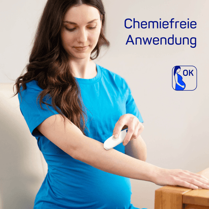 A pregnant woman in a blue shirt uses the HARTMANN insect bite healer | Pack (1 piece) by Paul Hartmann AG on her arm, with the text "chemical-free application" and a logo as a release signal. She stands in a softly lit room.