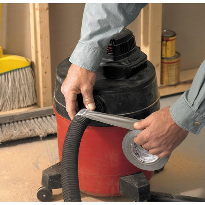 A person wraps Scotch® Universal Tape 2904 (50 m x 48 mm) from 3M Deutschland GmbH around a vacuum cleaner hose attached to a red shop vacuum. In the background, a broom and paint cans are visible.