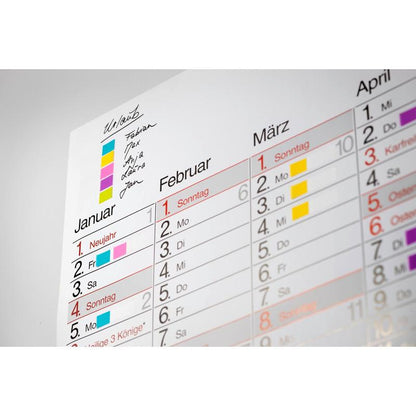 A German wall calendar for January-March shows various appointments color-coded with a key, handwritten notes, and the Post-it® Index Flags Mini and Index Arrows from 3M Deutschland GmbH in blue and yellow in the upper left corner.