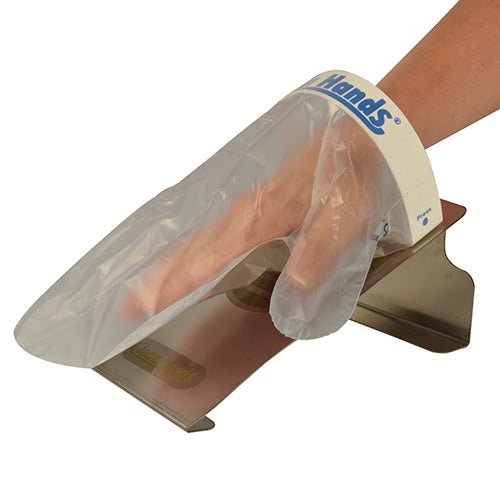 A hand wears a disposable plastic glove from the PAPSTAR Clean Hands Base Kit (stainless steel, 11.5x12.7x22 cm, silver), which is labeled "Clean Hands" on the cuff for hygienic cleanliness. The glove is taken from a box assembled by PAPSTAR GmbH (1 piece).