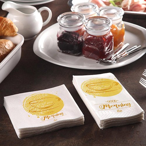 A breakfast table with croissants, a pot, and 200 PAPSTAR napkins (3-ply 1/4-fold, 24x24 cm) from PAPSTAR GmbH with the inscription "Good Morning", along with jars of jam and three forks for a cozy breakfast.