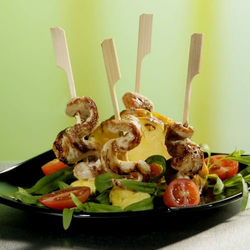 The PAPSTAR 250 finger food skewers "pure" by PAPSTAR GmbH are served with grilled chicken and pineapple on greens with cherry tomatoes on a black plate - ideal for any party buffet.