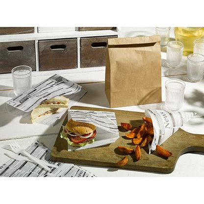 A table with a sandwich, a burger, and potato wedges, wrapped in PAPSTAR 5 wrapping papers 3 cm x 2 cm "Newsprint" from PAPSTAR GmbH, next to a brown paper bag, plastic cups and cutlery, and a wooden serving board on a white surface.