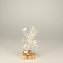 A PAPSTAR 300 bottom bag, cellophane "pure" transparent from PAPSTAR GmbH holds gold-wrapped candies tied with a light ribbon on a plain background – an elegant, sustainable touch with biodegradable packaging.