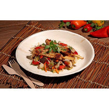 Grilled chicken skewers with a colorful vegetable pan are served on a PAPSTAR 6 plate, palm leaf "pure" round by PAPSTAR GmbH - environmentally friendly tableware, stylishly presented on a woven mat with wooden cutlery and fresh bell peppers in view.