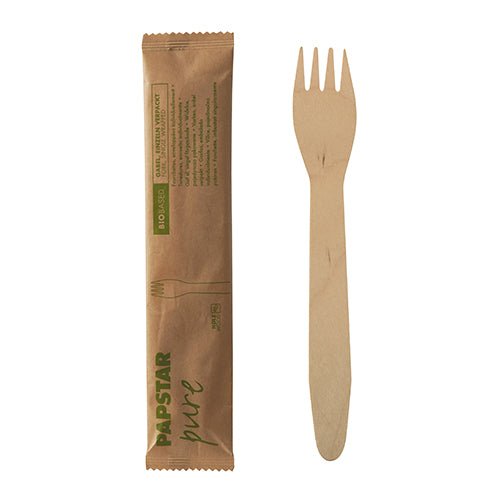 A PAPSTAR wooden fork "pure", 15.5 cm, individually wrapped in shrink film (50 pieces), lies next to its unopened brown packaging from PAPSTAR GmbH with green print and simple design.