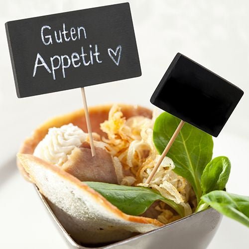 A small bowl holds a rolled slice of meat, greens, crispy onions, and cream. Two PAPSTAR finger food picks 8.5 cm (black, pack of 20) from PAPSTAR GmbH are the ideal addition to any buffet or party accessory collection.