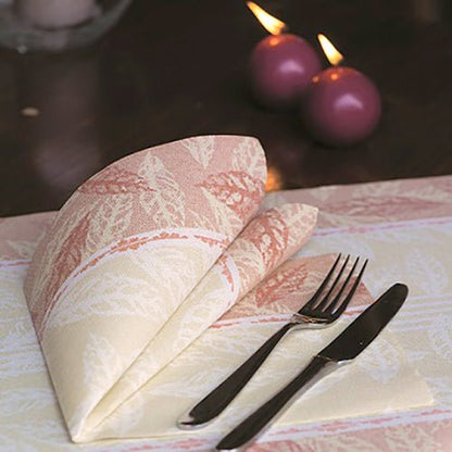 A folded red napkin PAPSTAR 50 napkins "ROYAL Collection" 1/4-fold 40 x 40 cm by PAPSTAR GmbH lies next to a fork and knife on a set table. In the background, two burning purple candles can be seen.