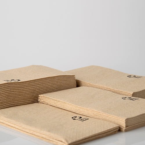 Four stacks of PAPSTAR napkins, 3-ply, 33x33 cm, natural, made from recycled paper (100 pieces) by PAPSTAR GmbH lie on a white surface. Each recycled napkin is marked with a small black recycling symbol in the corner.
