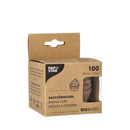 A brown box from PAPSTAR GmbH with the label "PAPSTAR 100 baking cups round" contains 100 bio-based baking cups (5 x 3 cm). The front shows a cupcake illustration, the trilingual product name, and a window that displays the cups inside.