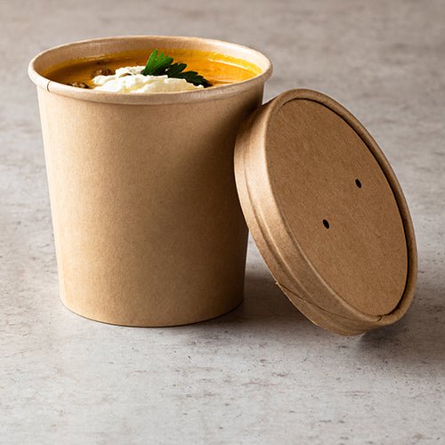 A Starpak 25 soup cup, round cardboard 470 ml in brown stands without a lid on a light gray countertop, revealing a creamy orange soup garnished with cream and parsley – an eco-friendly choice for your meal.