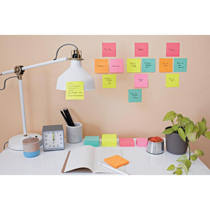 A tidy desk with a lamp, clock, plant, pen holder, an open notebook, and pens. On the wall above the desk, colorful Post-it® Notes Cubes Ultra Colors from 3M Deutschland GmbH are attached for handwritten reminders and tasks.