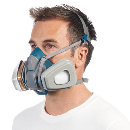 A man with short brown hair in a white shirt wears a 3M™ Quick Latch Respirator 6502QLKIT-1 from 3M Deutschland GmbH with a replaceable filter (A2P3) for organic vapors and adjustable headbands.