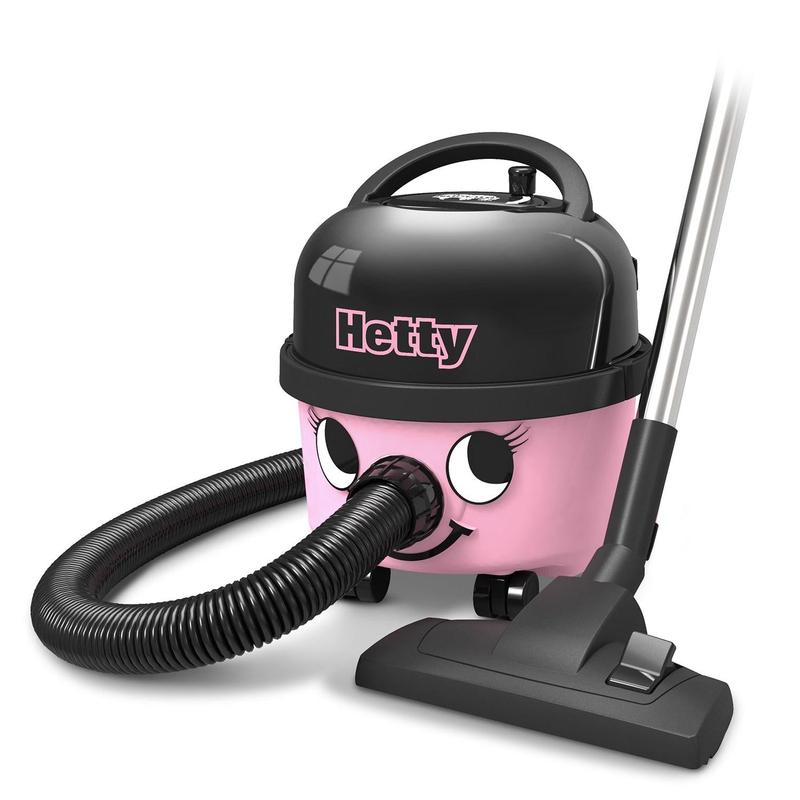 The Hetty Compact Vacuum Cleaner HET160-11 from Numatic International GmbH is a pink and black canister vacuum with a smiling face, a flexible hose, a mobile base, and a suction head that stands on the floor next to the device.