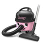 The Hetty Compact Vacuum Cleaner HET160-11 from Numatic International GmbH is a pink and black canister vacuum with a smiling face, a flexible hose, a mobile base, and a suction head that stands on the floor next to the device.