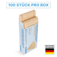 A box with the label "ARNOMED WOODEN SPATULA Unsterile natural" by ARNOWA GmbH contains 100 disposable wooden spatulas. At the top, the text "100 PIECES PER BOX" is displayed, with a German flag at the bottom right and "GERMAN COMPANY Practice Needs".
