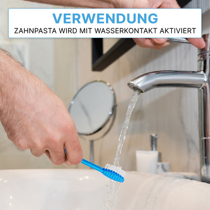A person holds an ARNOMED disposable toothbrush with toothpaste from ARNOWA GmbH under running water from a bathroom faucet. In the background, there is a mirror and the faucet. The German text indicates that the toothpaste is activated upon contact with water. Box: 100 pieces.
