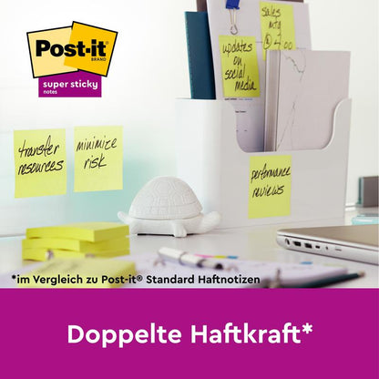 On a desk, there is a white organizer from 3M Deutschland GmbH, papers, pens, and Post-it® Super Sticky Notes (76 mm x 76 mm, 90 sheets/block, 100% PEFC) with handwritten reminders on a glass wall. "Double the sticking power" and the logo are highlighted.
