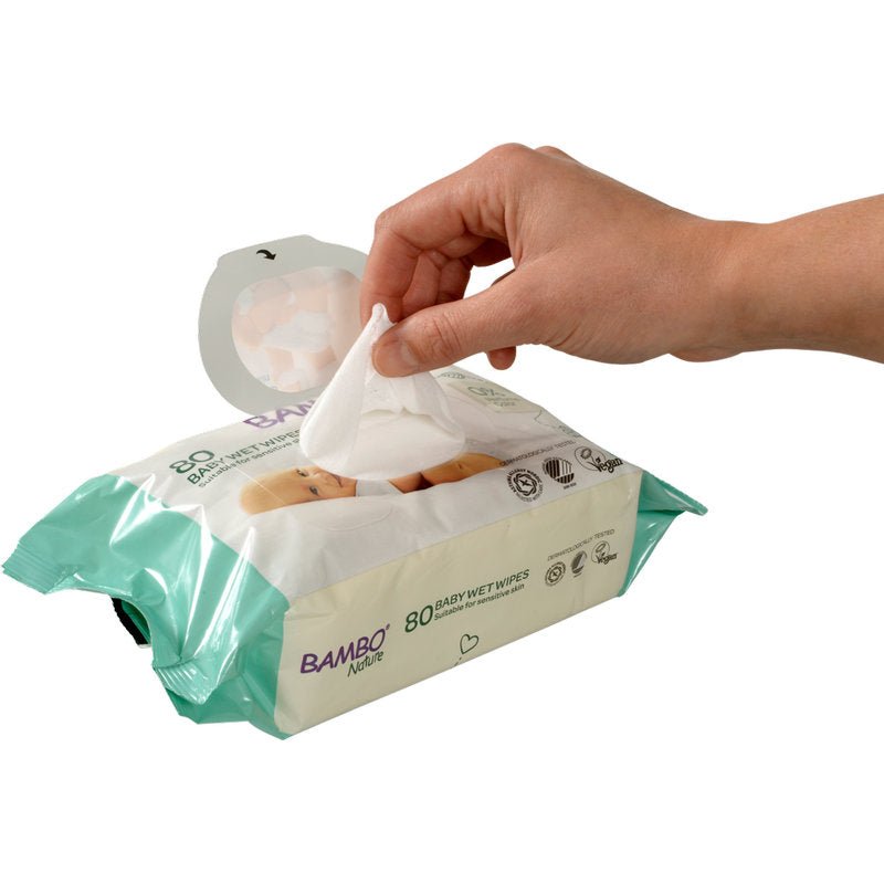 A hand pulls a Bambo Nature wet wipe with adhesive closure (15x20cm, 80 pieces) from Abena Re-Seller GmbH out of its light green-white packaging, which is designed for sensitive baby skin with icons and text on the front.
