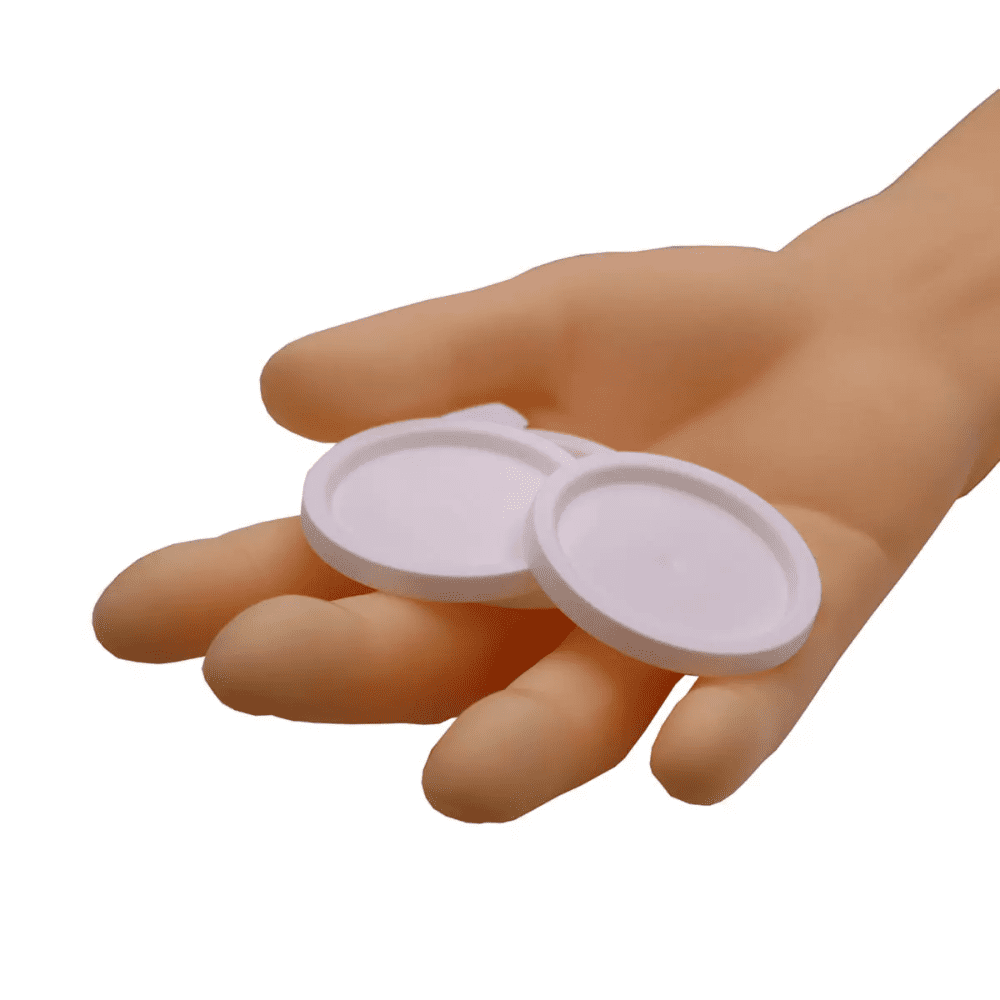 A hand holds two round AMPri lids for medicine cups, white objects against a plain white background.