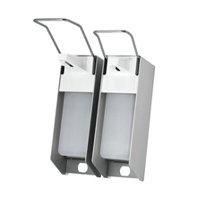 Displayed are two AMPri wall dispensers for 500 ml disinfectant and soap, with a stainless steel housing and a white plastic dispenser. Each is equipped with a long lever for hygienic dispensing. They are placed side by side against a plain white background.