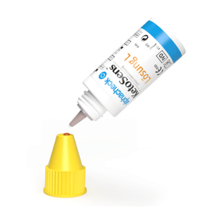A white bottle with a blue-yellow label is turned upside down, with the dropper nozzle sitting over a yellow cap. The label contains text and symbols indicating that it is likely a product Alphacheck KetoSens β-Ketone Control Solution L+M | Package (2 bottles) by Berger Med GmbH for use with keto measuring devices.