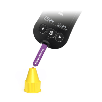 A digital measuring device with a display showing “09:24” and “12:37 PM” is used to test a purple strip labeled “Alphacheck KetoSens β-Ketone Control Solution L+M | Package (2 bottles)”. The strip Alkacheck Alphacheck KetoSens β-Ketone Control Solution L+M | Package (2 bottles) points to a small yellow cap. The device features a large “S” button below the display.