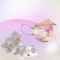A particle-filtering Altruan designer face mask that meets the FFP2 standard shows its ergonomic fit against a pastel background with a pink-green gradient. In the foreground, a cluster of white orchids highlights the elegance of its stylish design.