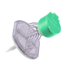 The B. Braun Mini-Spike® V with valve from B. Braun Deutschland GmbH & Co. KG is presented in a heart-shaped form with a transparent body and green tip. It features an integrated valve for additional functionality and has a sharp tip at the bottom for attaching objects to surfaces.