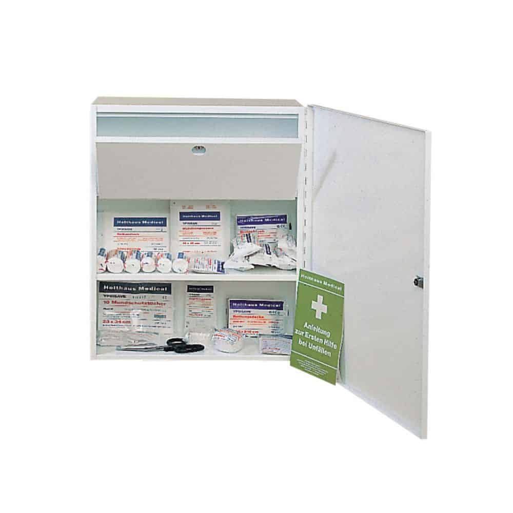 A white metal first aid cabinet, the *Holthaus Medical First Aid Cabinet MEDICUS*, displays various medical items neatly arranged on two shelves when the door is open. The items include adhesive bandages, gauze compresses, antiseptic wipes, scissors, a first aid manual, and a lockable medication compartment.