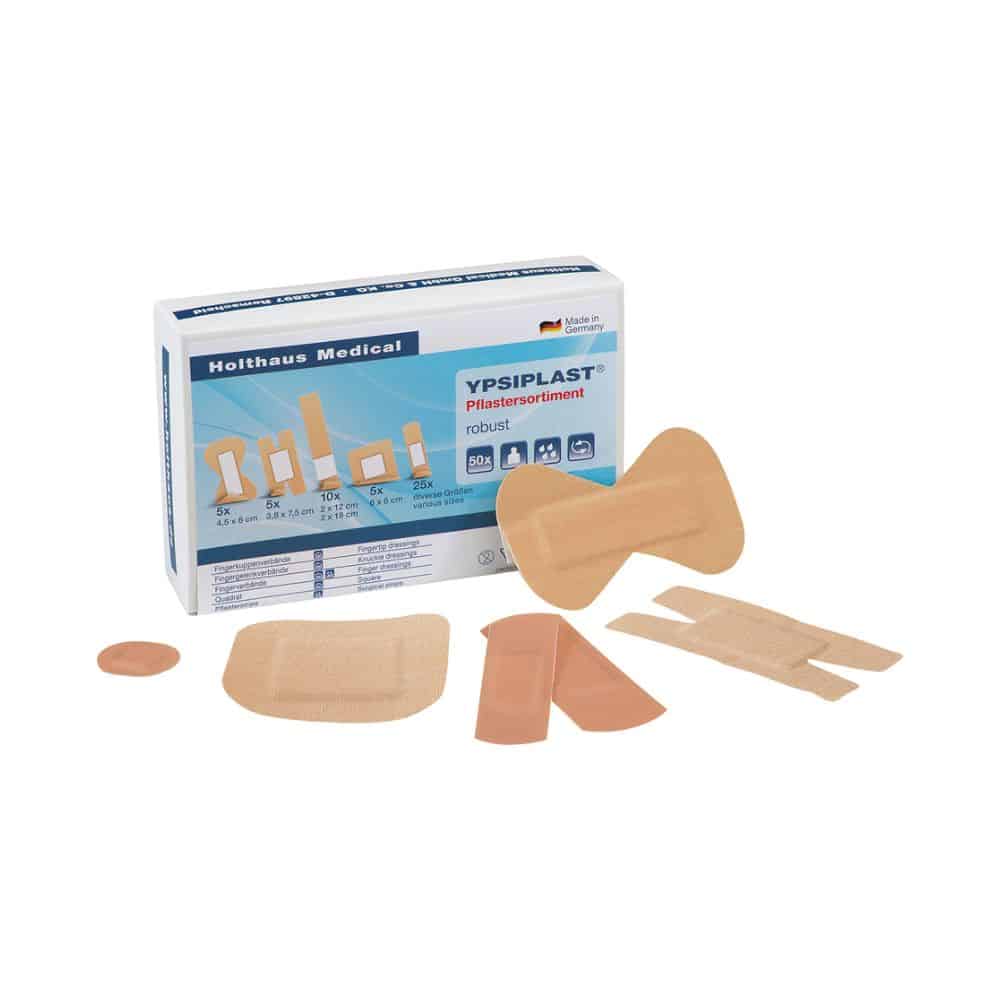 The image shows an opened box of the YPSIPLAST® plaster assortment robust | Pack (50 pieces) from Holthaus Medical GmbH & Co. KG. In front of the packaging, plasters in various shapes, including round, square, and rectangular designs, are arranged.