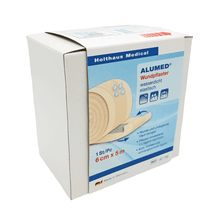 A white box of Holthaus Alumed® wound plaster, 6 cm x 5 m from Holthaus Medical GmbH & Co. KG shows an image of the plaster roll and states that it is hypoallergenic, waterproof, and elastic. The text on the box of the water-repellent wound plaster is mainly in German. The product is made in Germany.