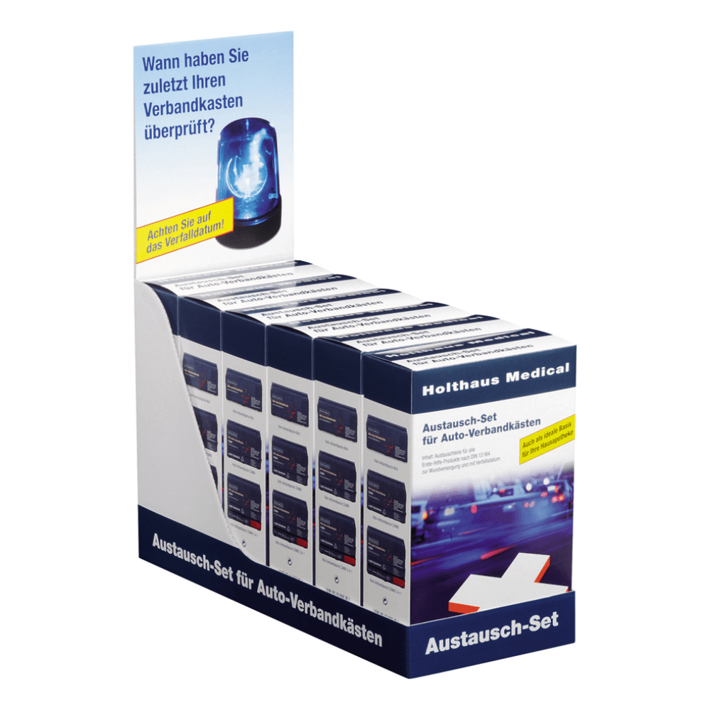At an exhibition stand, there are several boxes labeled “Holthaus Replacement Set for Car First Aid Kits DIN 13157 | Package (1 piece)“ by Holthaus Medical GmbH & Co. KG. The stand features a header with the image of a blue emergency light and a German text urging the viewer to remember the last time they checked their first aid products or car first aid kits.