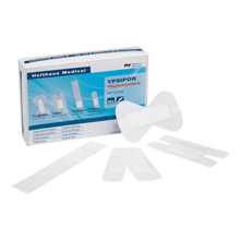 The image shows a box of Holthaus Ypsipor plaster assortment sensitive (50-piece) adhesive plasters by Holthaus Medical GmbH & Co. KG. In front of the box, several white wound plasters in different shapes and sizes are depicted, labeled with "plaster assortment sensitive skin". The box contains 50 pieces.