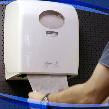 A person pulls paper towels from a wall-mounted Aquarius™ Slimroll™ roll towel dispenser - White from Kimberly-Clark GmbH, which features an illustrated guide and a modern design against a dark, dotted wall.