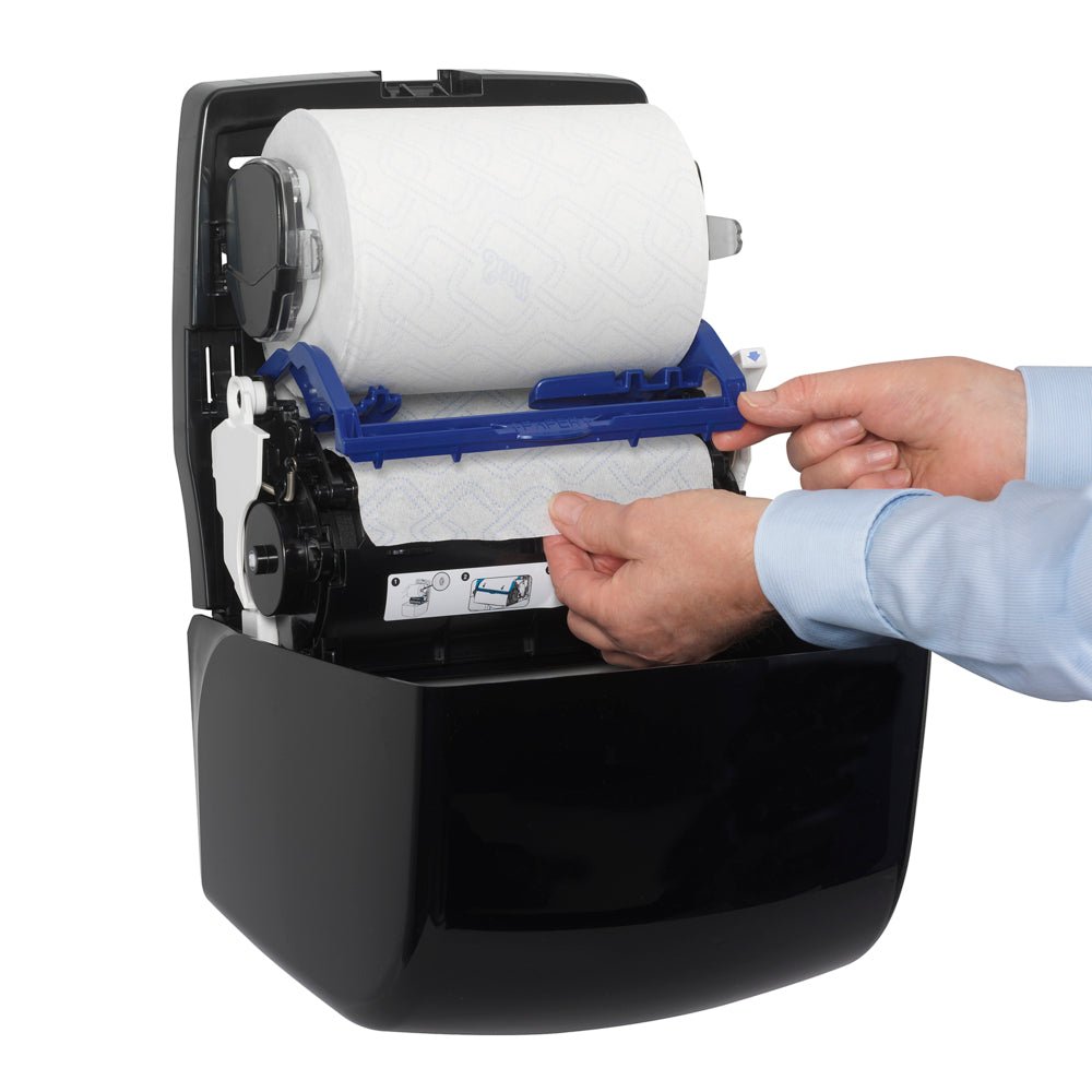 A person in a blue shirt inserts a paper towel roll into a Kimberly-Clark GmbH Aquarius™ Slimroll™ roll towel dispenser - Black and carefully threads the paper for hygienic dispensing.