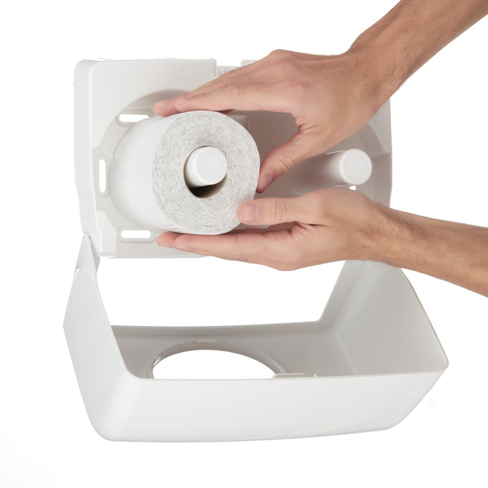 A person places a new roll of Kleenex® toilet paper small rolls from an 8 x 12 pack by Kimberly-Clark GmbH into a white plastic dispenser with an open lid.
