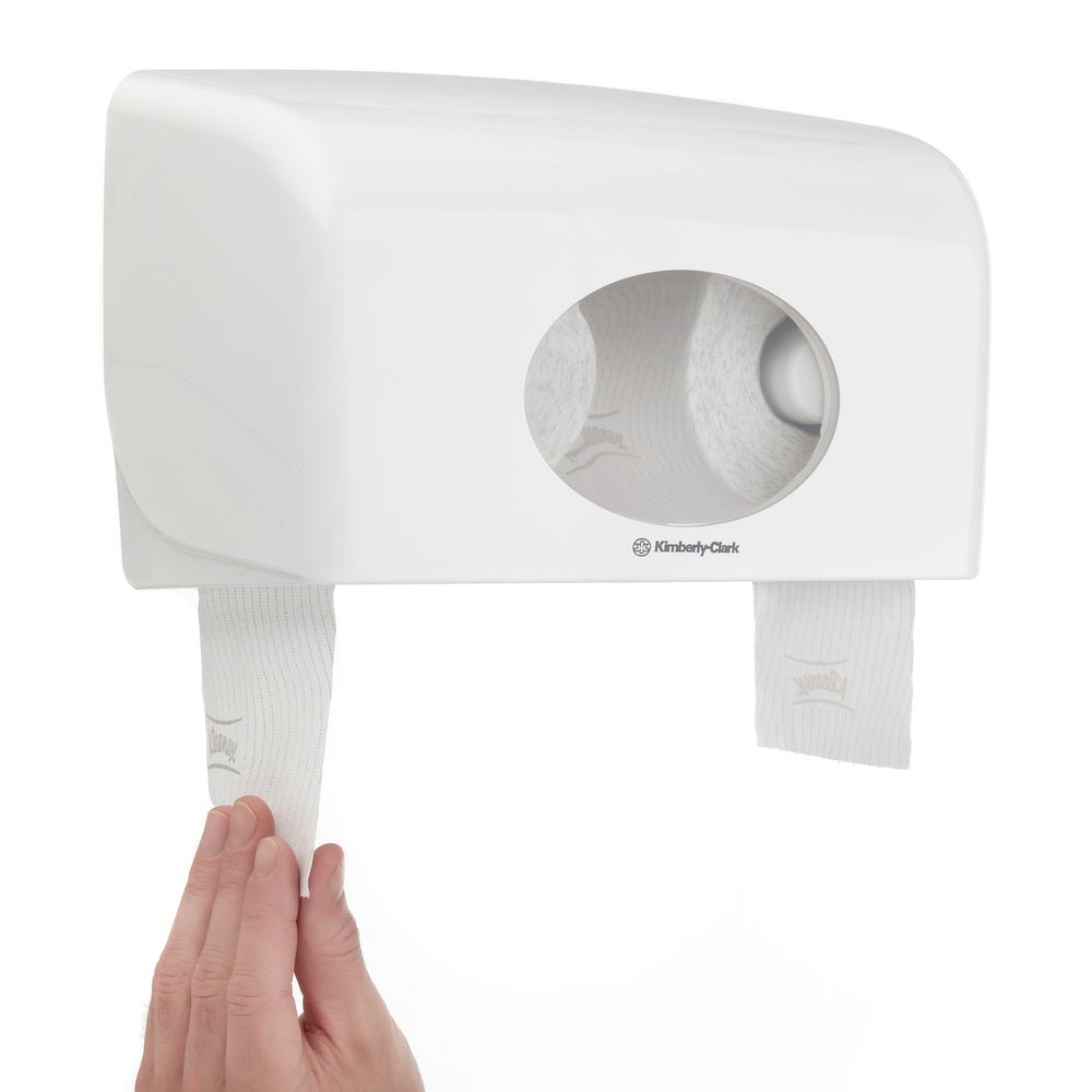 A hand pulls the Kimberly-Clark GmbH Kleenex® toilet paper rolls (white, 8 pack x 12 small rolls, each 250 sheets) from a double-wall dispenser with an oval window - ideal for use with this carton (8 packages).