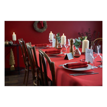 A dining table is set with Dunicel tablecloth rolls (1.18 m x 10 m) from Duni GmbH and matching napkins, white plates, wine glasses, candles, and a menu card. Brown chairs surround the table against red walls with festive Christmas decorations – perfect for large events.